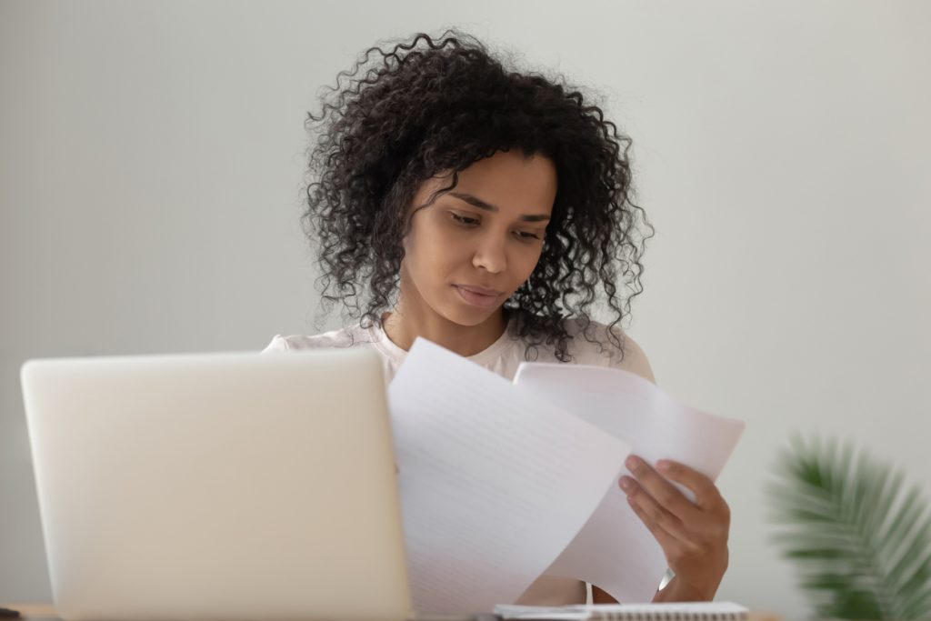 Focused black girl read paperwork studying on laptop