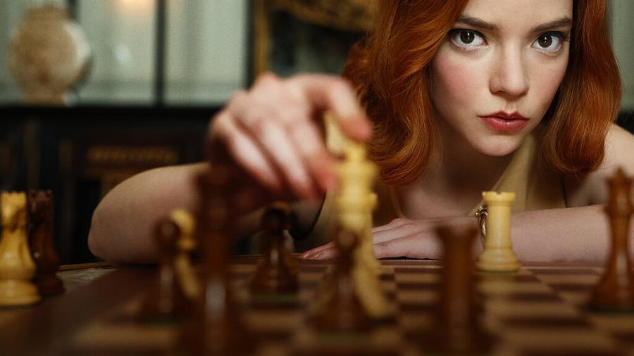 Imagem do filme "O Gambito da Rainha", em que uma mulher ruiva segura uma peça de xadrez simulando uma jogada.